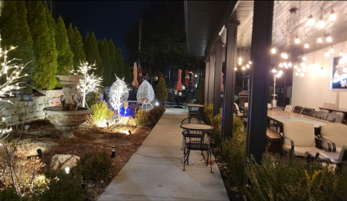 A well-lit outdoor patio with seating, decorative lights, and a garden path at night.